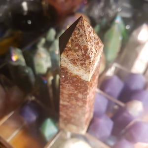 May include: A red and white crystal point with a rough, textured surface. The point is surrounded by other crystals in various colors.