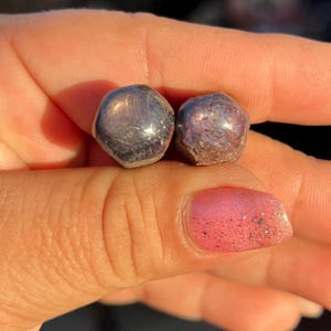May include: Two faceted gemstones, one is a dark gray and the other is a deep purple-red.