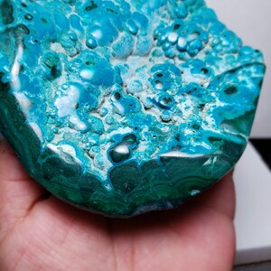 May include: A large, teal blue and green, polished, natural, gemstone with a bubbly, textured surface. The gemstone has a smooth, rounded edge.
