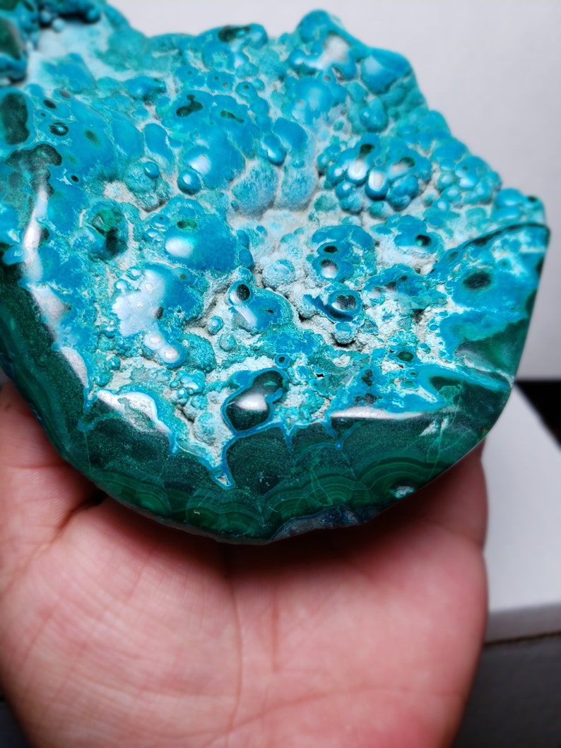 May include: A large, teal blue and green, polished, natural, gemstone with a bubbly, textured surface. The gemstone has a smooth, rounded edge.