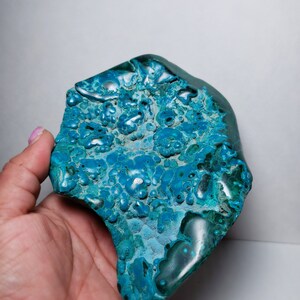 May include: A teal blue and green gemstone with a unique, bubbly texture. The stone has a rough, natural shape and is a beautiful example of a natural mineral.