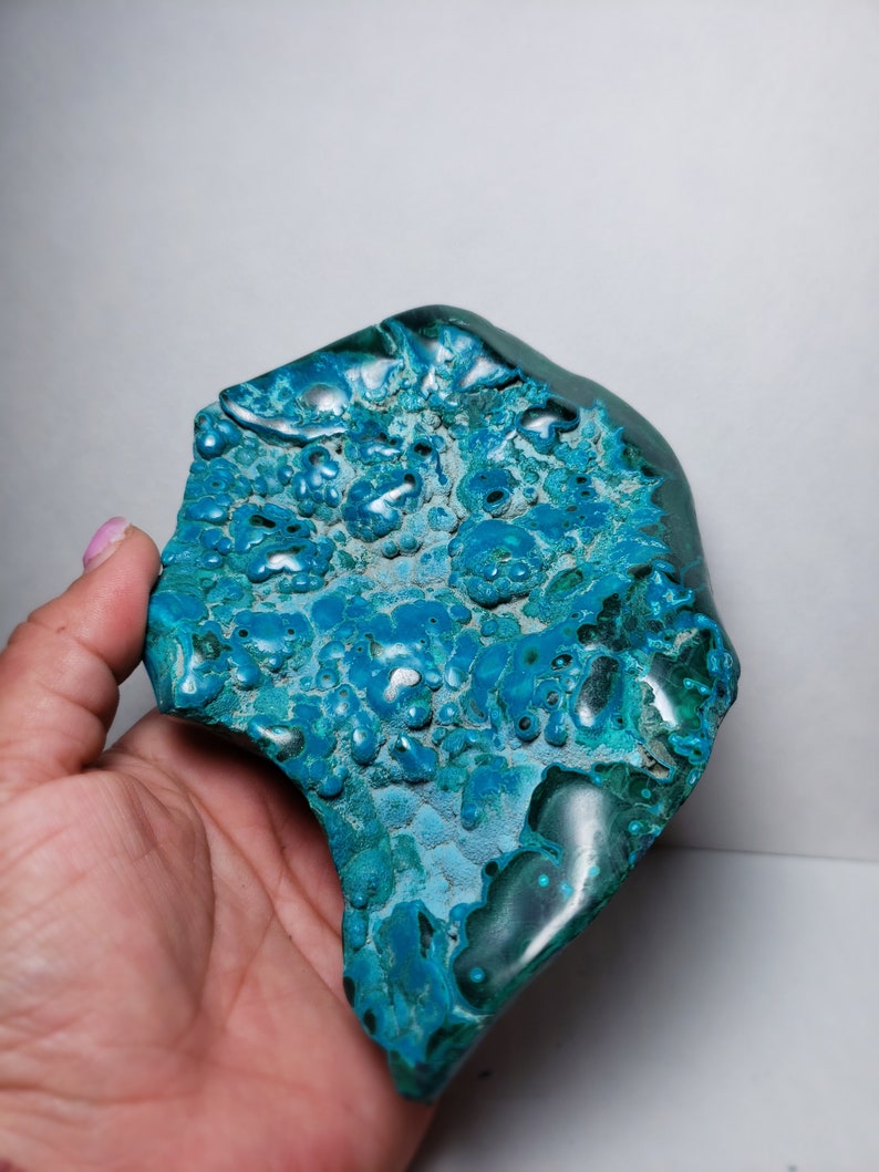 May include: A teal blue and green gemstone with a unique, bubbly texture. The stone has a rough, natural shape and is a beautiful example of a natural mineral.