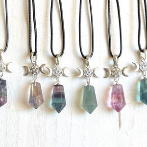May include: A collection of six necklaces with black cords. Each necklace features a silver-toned pendant with a crescent moon and star design, and a colorful, faceted crystal pendant in shades of purple, green, and blue.