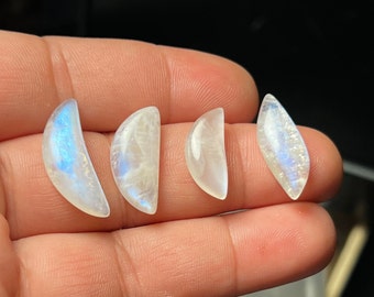 May include: Four crescent-shaped moonstone cabochons in various sizes, with iridescent blue and white colors.