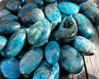 May include: A collection of smooth, polished blue apatite stones. The stones are oval shaped and have a light blue color with darker blue veins running through them.