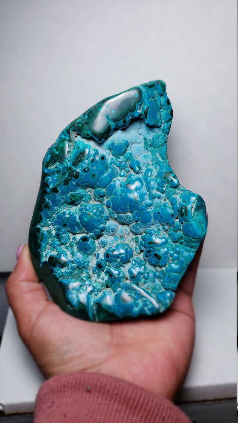 May include: A large, irregularly shaped piece of blue and green chrysocolla. The stone has a smooth, polished surface with a swirling pattern of blue and green.