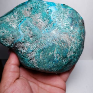 May include: A large, irregularly shaped, teal blue and silver gemstone. The gemstone has a rough, textured surface.