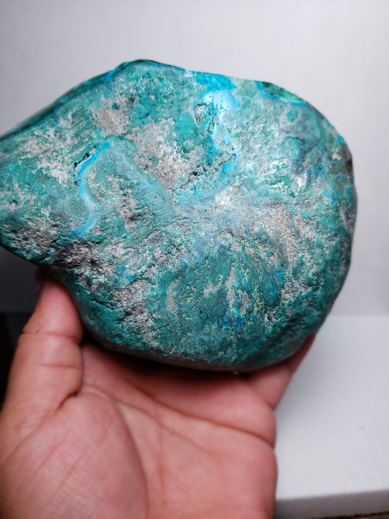 May include: A large, irregularly shaped, teal blue and silver gemstone. The gemstone has a rough, textured surface.