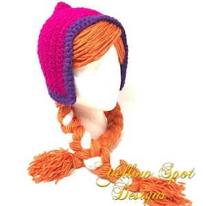 May include: A handmade crochet hat in bright pink with a purple trim and orange yarn braids. The hat is designed to resemble a character's hairstyle. The hat has a pointed top and is displayed on a white mannequin head.