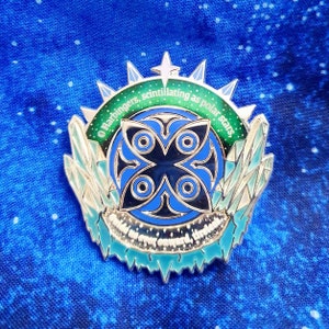 May include: A silver enamel pin with a blue and black design. The pin features a stylised four-pointed star with a circle around it. The text around the star reads "O harbingers, scintillating as polar stars".