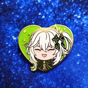 Può includere: Spilla a forma di cuore in smalto con un personaggio anime sorridente con capelli bianchi e dettagli verdi. La spilla ha un bordo dorato ed è posta su uno sfondo a cuore verde con stelle dorate.