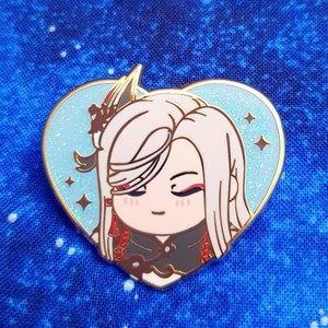 May include: A heart-shaped enamel pin featuring a cartoon character with long white hair, wearing a black and red outfit. The pin has a glittery blue background with gold accents.