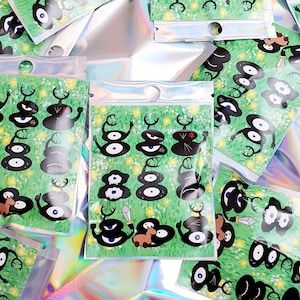 May include: A set of stickers featuring cartoon characters with multiple eyes on a green background with white flowers. The characters are black and white with red accents. The stickers are packaged in clear plastic bags.