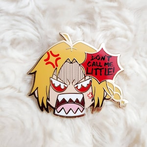 May include: Gold-coloured enamel pin featuring an angry cartoon character with yellow hair and a red speech bubble that says "Don't call me little!"