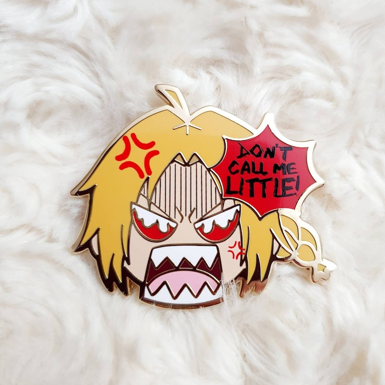 May include: Gold-coloured enamel pin featuring an angry cartoon character with yellow hair and a red speech bubble that says "Don't call me little!"