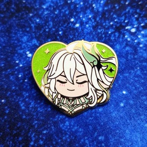 Può includere: Spilla a forma di cuore in smalto con un personaggio dei cartoni animati con capelli bianchi e dettagli verdi. La spilla ha un bordo dorato e uno sfondo verde con dettagli a stella. Il personaggio ha un'espressione serena.