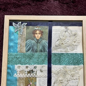 Puede incluir: Un collage de técnica mixta enmarcado en forma cuadrada que presenta un retrato central de una persona con vestido azul, superpuesto con cinta de purpurina verde azulado, tiras de terciopelo azul oscuro, apliques florales de encaje blanco con perlas.