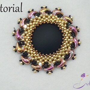May include: A close-up of a beaded jewelry piece with a black center and a gold and pink beaded border. The piece is circular and has a delicate, intricate design.
