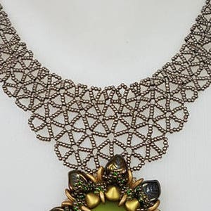 May include: A silver beaded necklace with a large, green and gold beaded flower pendant. The pendant has a green glass center and is surrounded by gold and green beads.