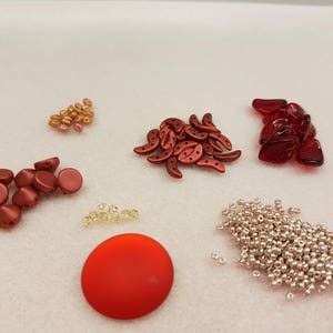 May include: Assortment of red, orange, and gold beads, including round, crescent, and teardrop shapes. There are also silver beads and a large red disc.