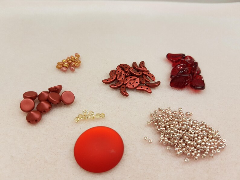 May include: Assortment of red, orange, and gold beads, including round, crescent, and teardrop shapes. There are also silver beads and a large red disc.