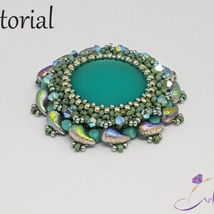 May include: A turquoise green cabochon surrounded by a beaded border of gold, green, and iridescent beads. The beads are arranged in a circular pattern, creating a decorative design.