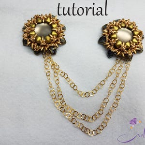 May include: Two gold and gray beaded flower brooches with a chain attached to each. The brooches are connected by a long gold chain.