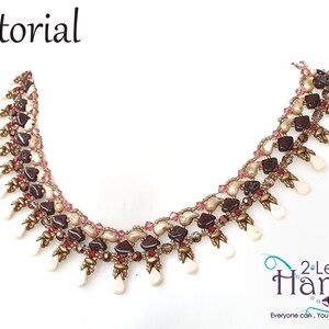 May include: A beaded necklace with a multi-colored design featuring brown, pink, and white beads. The necklace has a fringe of white beads at the bottom. The text "2 Left Hands" is visible in the lower right corner of the image.