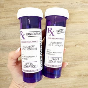 Może przedstawiać: Dwa fioletowe butelki po lekach z białymi zakrętkami, z napisem "Hangover Kit". Etykiety głoszą "Lifelong Memories That Will Last a Lifetime" i "30. urodziny Tayli".