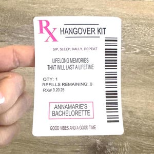 May include: A white rectangular card with pink text and a barcode. The card reads "HANGOVER KIT" and includes the phrases "SIP, SLEEP, RALLY, REPEAT" and "LIFELONG MEMORIES THAT WILL LAST A LIFETIME". It also says "ANNAMARIE'S BACHELORETTE".