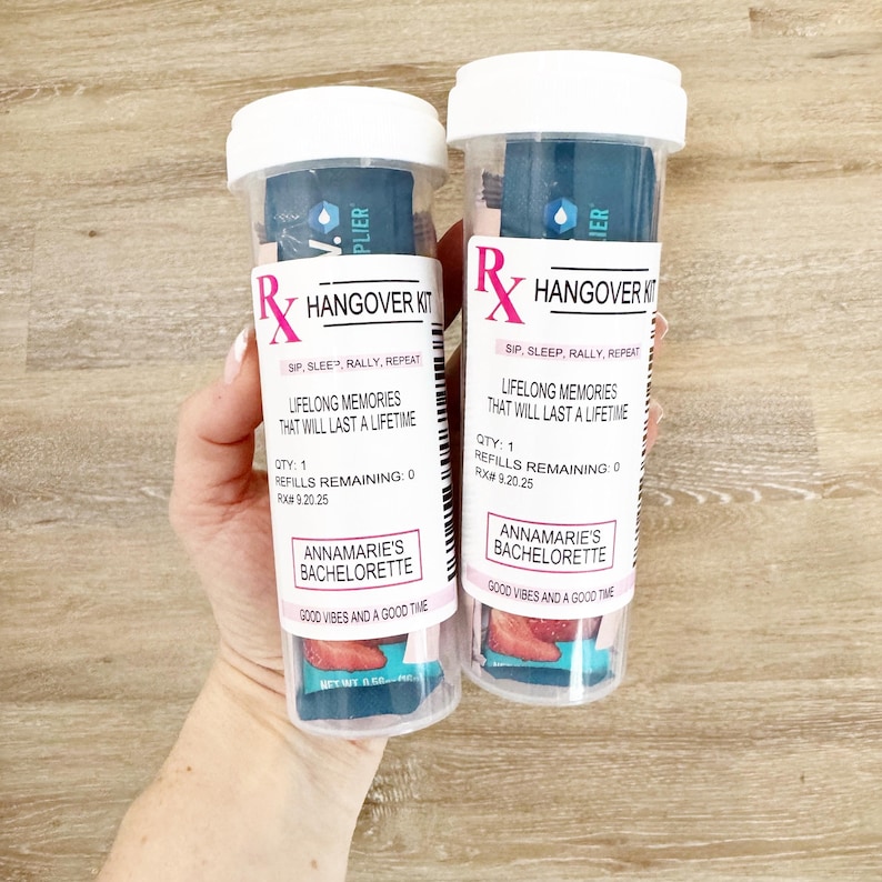 Może przedstawiać: Dwie przezroczyste plastikowe tuby z białymi wieczkami, oznaczone jako "Rx Hangover Kit". Tuby zawierają niebieską i białą zawartość oraz tekst "Lifelong Memories That Will Last a Lifetime". Na dolnej etykiecie napisano "Annamarie's Bachelorette" i "Good Vibes and a Good Time."