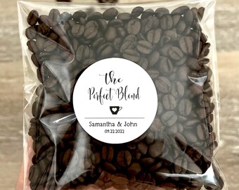 Może przedstawiać: Przezroczysta plastikowa torba wypełniona ciemnobrązowymi ziarnami kawy. Biała okrągła etykieta głosi "The Perfect Blend" z ikoną filiżanki do kawy oraz imionami "Samantha & John" z datą "09.22.2022".