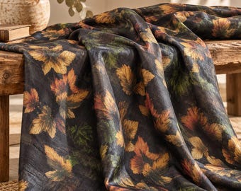 May include: A dark fabric runner featuring a repeating pattern of autumn leaves in shades of yellow, orange, and green. The textile is draped over a wooden surface, showcasing a textured appearance with a rich, deep black background color.