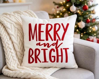 May include: A square white throw pillow featuring the red embroidered text MERRY and BRIGHT centered on the front. The lettering uses a combination of bold block capitals and a cursive script font for the word and, creating a festive look.
