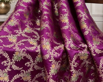 May include: A vibrant magenta fabric featuring an intricate woven pattern of gold, light green, and yellow floral motifs. The textile displays a dense, repeating design of scrolling vines and blossoms that create a textured, shimmering appearance.