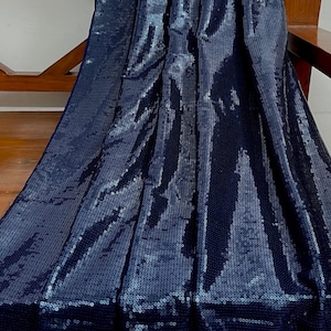 Puede incluir: Primer plano de una tela azul oscuro con lentejuelas. Las lentejuelas están dispuestas en un patrón que crea un efecto brillante.