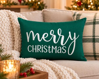 Può includere: Un cuscino rettangolare verde scuro con il testo ricamato in bianco merry CHRISTmas, caratterizzato da un mix di caratteri corsivi e stampatello. Il cuscino presenta una finitura in tessuto liscio ed è l'elemento decorativo centrale.