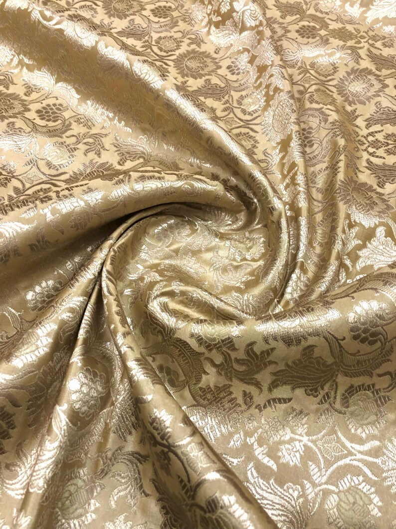 May include: Close-up of a golden fabric with a floral pattern. The fabric has a shiny, textured surface with intricate details in a lighter gold color. The folds and drapes of the fabric create shadows and highlights, enhancing the visual texture.