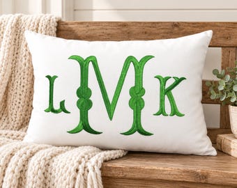 May include: A rectangular white throw pillow featuring a large, centered, embroidered monogram in a vibrant green thread. The monogram consists of the letters L, M, and K, with the central letter M being significantly larger than the L and K.