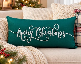 May include: A rectangular dark green throw pillow featuring the white embroidered text Merry Christmas in a cursive script font. The pillow is positioned horizontally and displays a smooth fabric texture with clean, finished edges.