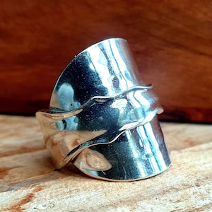 Peut inclure: Une bague en argent fabriquée à partir d'une cuillère recyclée, avec un design ondulé. La bague est large et a un aspect unique et artisanal.