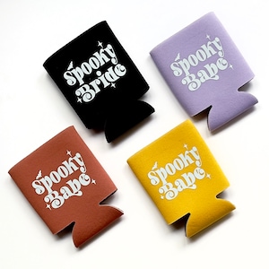 May include: Four different colored can coolers with the text "Spooky Babe" or "Spooky Bride" in white letters on a black, purple, brown, and yellow background.