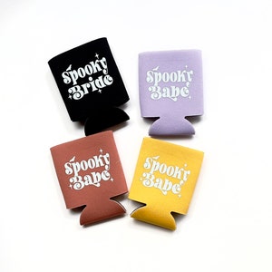 May include: Four different colored can coolers with the text "Spooky Babe" or "Spooky Bride" in white lettering.