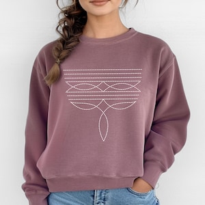 May include: A mauve colored sweatshirt with a white geometric design on the front. The design features a series of lines and curves that resemble a stylized flower.