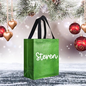 Op de afbeelding: Een groene herbruikbare boodschappentas met zwarte handvatten. De tas heeft de naam "Steven" in wit op de voorkant gedrukt.