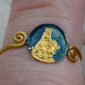 Könnte beinhalten: Goldfarbener Ring mit kreisförmigem blau-goldenem Emaille-Design. Das Design zeigt eine religiöse Figur. Der Ring hat dekorative Wirbel auf beiden Seiten des kreisförmigen Designs.