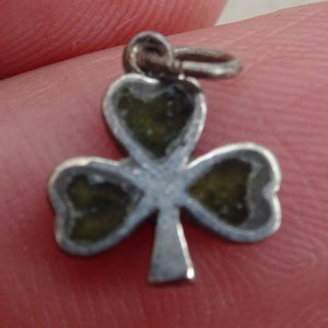 May include: A silver charm in the shape of a shamrock with green enamel. The charm has a loop at the top for attaching to a necklace or bracelet.