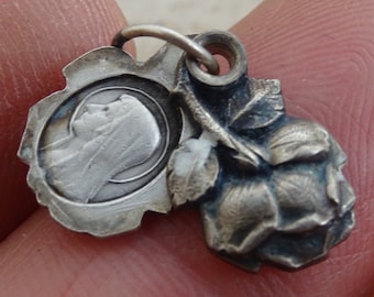 May include: Silver pendant charm featuring a detailed rose and a small oval medallion with a depiction of the Virgin Mary.