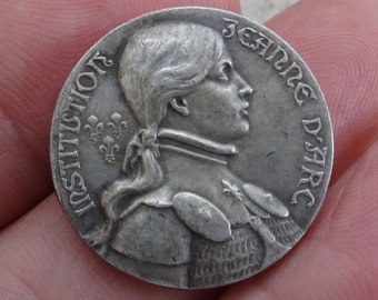Könnte beinhalten: Silbermünze mit einem Porträt von Jeanne d'Arc und der Inschrift "INSTITUTION JEANNE D'ARC".