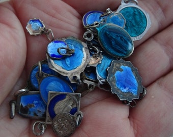 May include: A collection of vintage silver charms with blue enamel. The charms are in the shape of ovals, circles, and squares. Some of the charms have religious imagery.